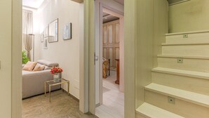 Un couloir avec un escalier, un canapé avec des coussins, une petite table avec un vase et des tableaux encadrés accrochés au mur.