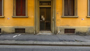 Un bâtiment à la façade jaune, avec une entrée centrale dotée d’une porte et deux fenêtres avec des volets.