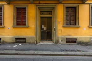 A building with a yellow facade, a central entrance with a door, and two windows with shutters.