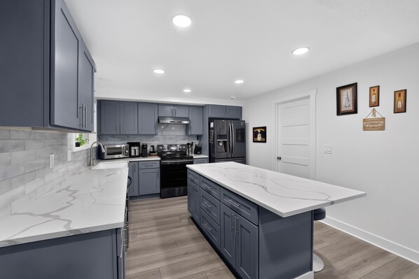 A modern kitchen with grey cabinets, a white marble countertop, stainless steel appliances, and a wooden floor. - Family Fairview Home | Gorge Access & Covered Deck (Fairview)