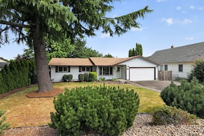 A single-story house with a garage, surrounded by a well-maintained lawn and various shrubs. - Family Fairview Home | Gorge Access & Covered Deck (Fairview)