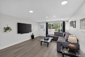 A modern living room with a flat-screen TV, a glass coffee table, a sofa, and a lamp. - Family Fairview Home | Gorge Access & Covered Deck (Fairview)
