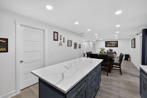 A modern kitchen with a marble countertop, dark cabinets, and a dining area with a table and chairs. - Family Fairview Home | Gorge Access & Covered Deck (Fairview)