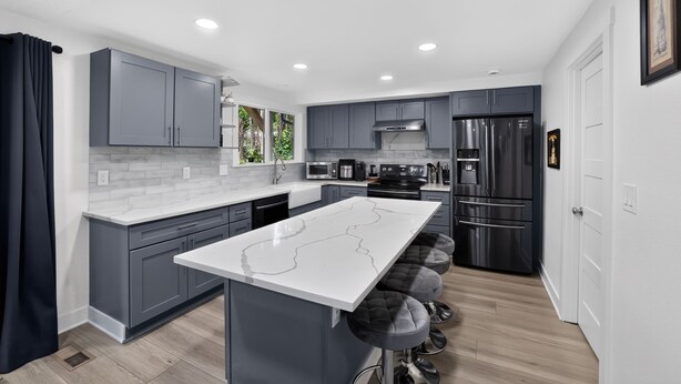 A modern kitchen with grey cabinets, a white island, and stainless steel appliances. - Family Fairview Home | Gorge Access & Covered Deck (Fairview)