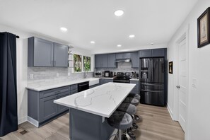 A modern kitchen with grey cabinets, a white island, and stainless steel appliances. - Family Fairview Home | Gorge Access & Covered Deck (Fairview)