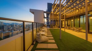 Eine moderne Dachterrasse mit Sitzgelegenheiten, Blick auf die Stadt und einem überdachten Bereich mit Lichterketten.