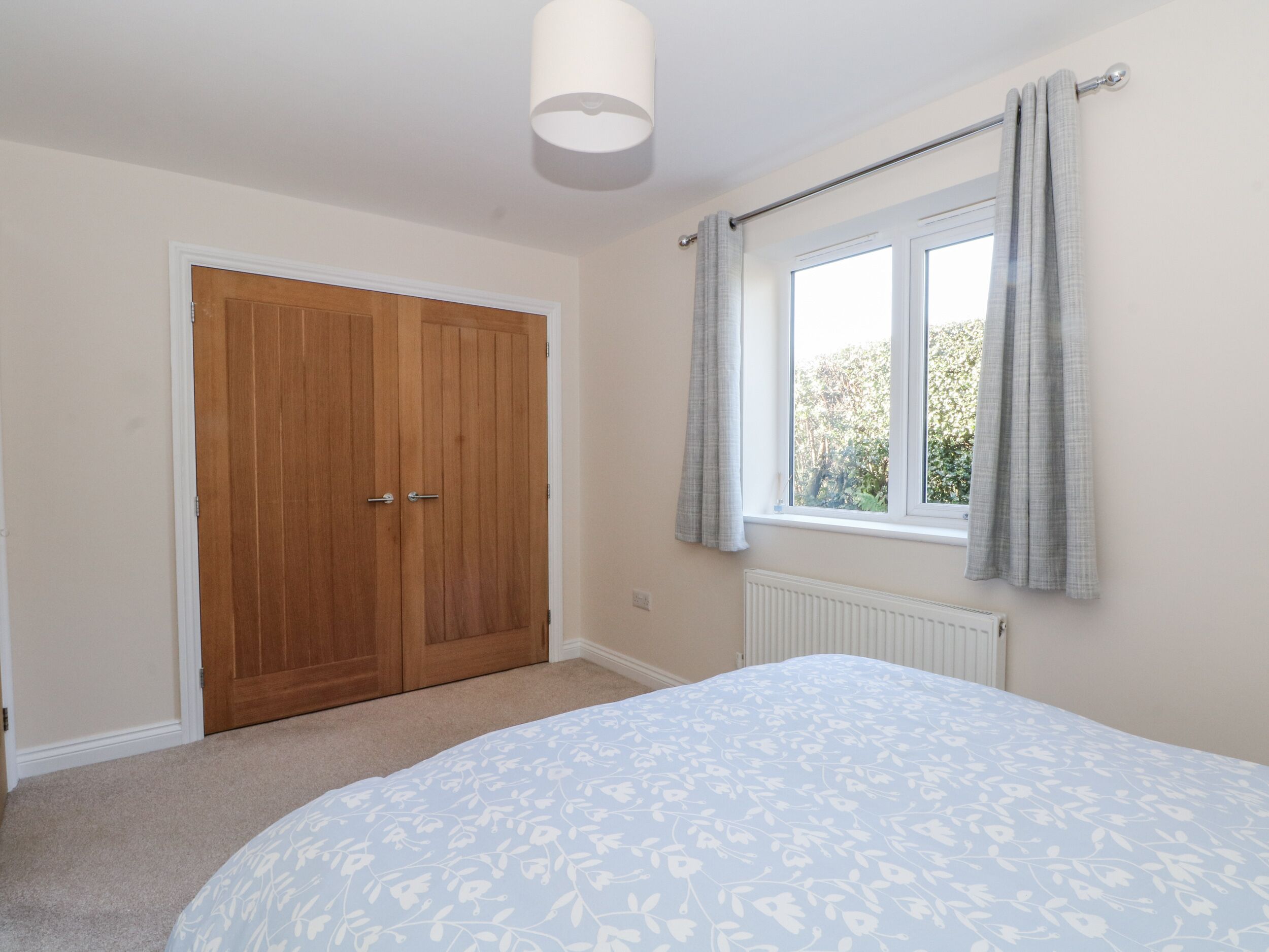 A bedroom with a double door, a window with curtains, a radiator, and a bed with a floral bedspread.