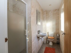 Ein Badezimmer mit Dusche, Waschbecken, Toilette und einer Holztür.