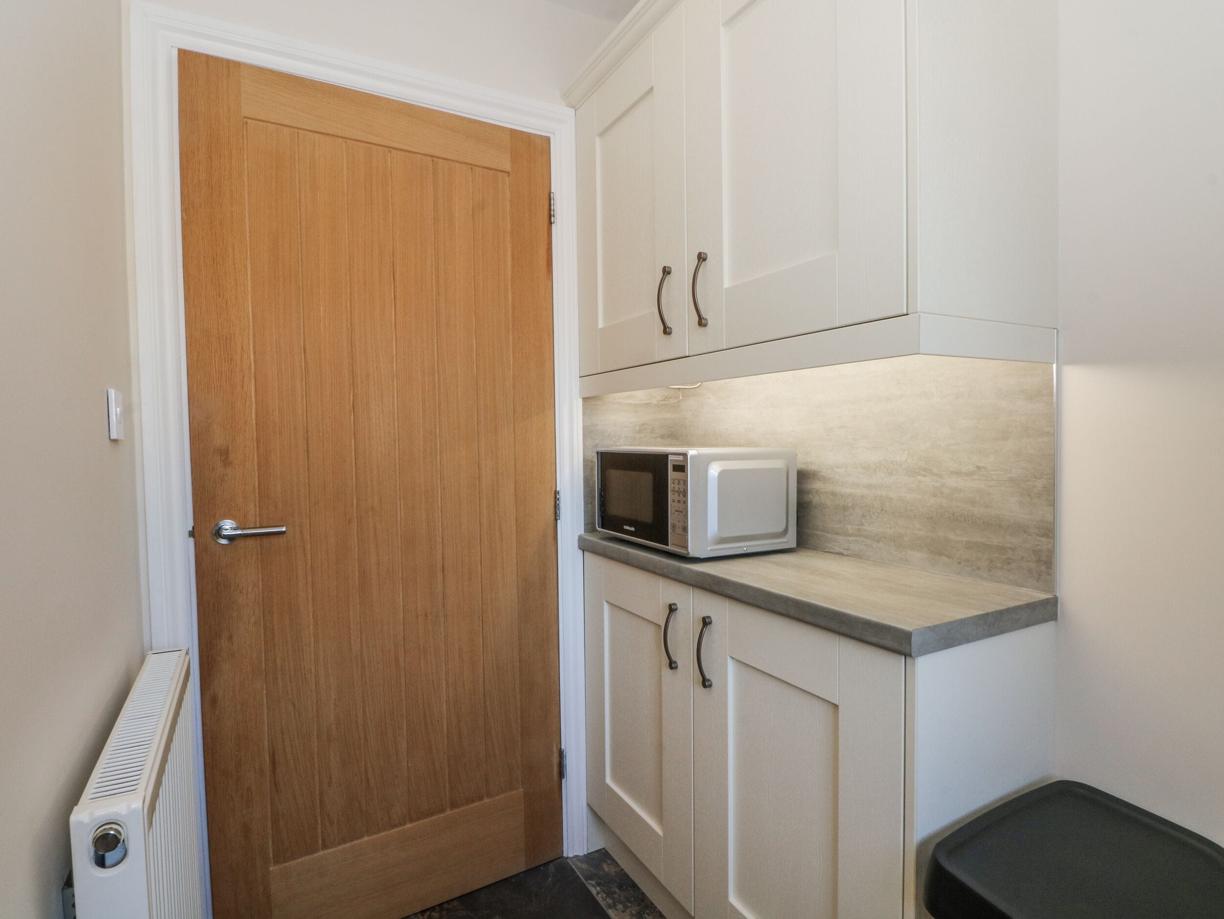 A compact kitchen with a wooden door, white cabinets, a microwave, and a radiator.