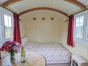 Una habitación acogedora con una cama, una mesa con un florero y dos ventanas con cortinas.