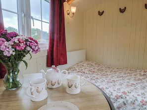 Ein Zimmer mit einer Holzvert äfelung, einer blumigen Tagesdecke, einer Vase mit rosa Blumen und einem Tisch mit weißen Tassen und einem Teekessel.