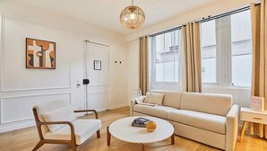 A living room with a sofa, armchair, coffee table, and a pendant light. - AN UNBEATABLE LOCATION IN THE HEART OF ONE OF PARIS'S MOST VIBRANT DISTRICTS (Paris)