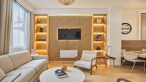 A modern living room with a sofa, armchair, coffee table, TV, and a dining area with a table and chairs. - AN UNBEATABLE LOCATION IN THE HEART OF ONE OF PARIS'S MOST VIBRANT DISTRICTS (Paris)