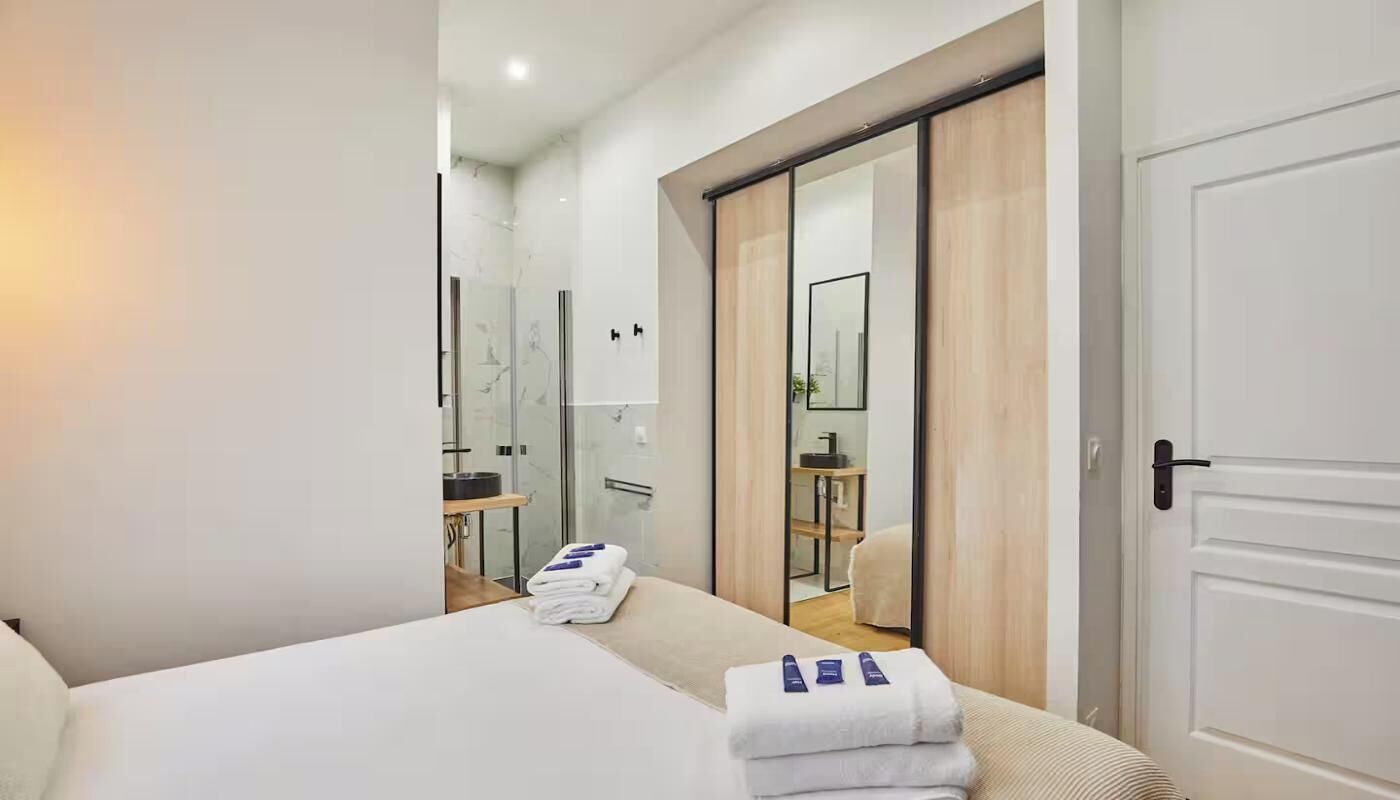 A hotel room with a bed, a bathroom with a shower, and a sliding door closet.