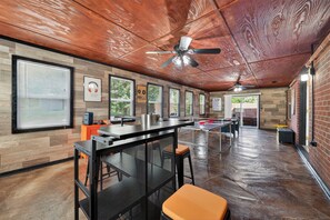 A spacious room with a wooden ceiling, a ceiling fan, a ping pong table, and a bar area with stools. - NEW! Southern Comfort Escapes 5BR for 14 Near NASA (Madison)