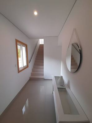 A modern interior with a staircase, a window, and a mirror. - Garden Hill R – Spacious Patio, Pool, Parking, Old Town (Albufeira)