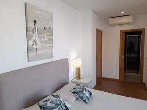 Une chambre d’hôtel comprenant un lit, une table de chevet avec une lampe, un climatiseur fixé au mur et une porte donnant sur une autre pièce.