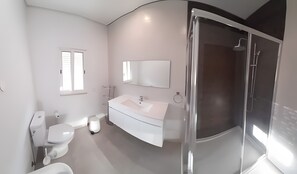 Une salle de bain moderne avec une douche à parois de verre, un lavabo blanc et des toilettes.