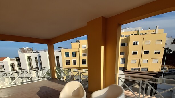 A balcony with white chairs, wooden flooring, and a view of yellow buildings. - Garden Hill R – Spacious Patio, Pool, Parking, Old Town (Albufeira)