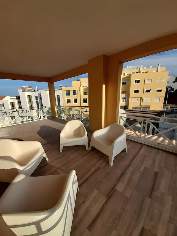 A balcony with white chairs, wooden flooring, and a view of yellow buildings. - Garden Hill R – Spacious Patio, Pool, Parking, Old Town (Albufeira)