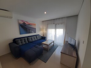 A modern living room with a sofa, a small table, a TV, and a painting on the wall. - Garden Hill R – Spacious Patio, Pool, Parking, Old Town (Albufeira)