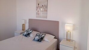 A bedroom with a large bed, two bedside tables, a wall-mounted artwork, and a nightstand with a lamp. - Garden Hill R – Spacious Patio, Pool, Parking, Old Town (Albufeira)