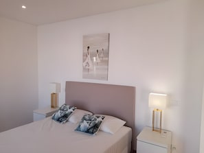 A bedroom with a large bed, two bedside tables, a wall-mounted artwork, and a nightstand with a lamp. - Garden Hill R – Spacious Patio, Pool, Parking, Old Town (Albufeira)