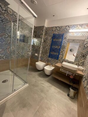 A bathroom with a glass shower enclosure, a sink, two toilets, and patterned tiles. - Tenuta Borgato Morelli (Veneto)