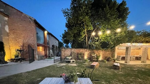 A backyard with a wooden table, a brick building, and string lights. - Tenuta Borgato Morelli (Este)