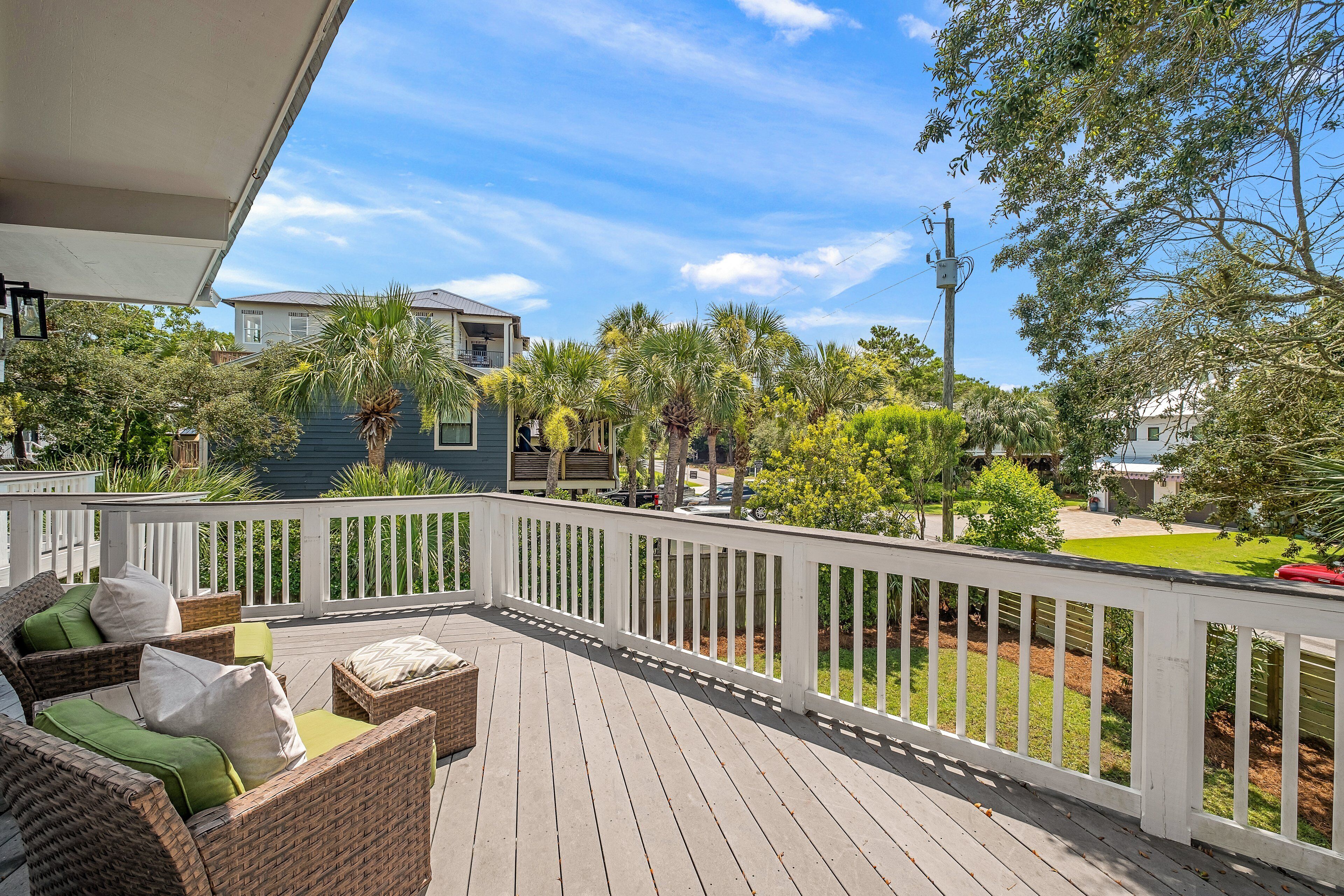 A wooden deck with wicker furniture, a white railing, and a view of neighboring houses and trees.