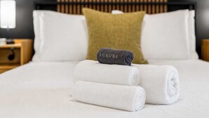 Een net opgemaakt bed met witte lakens, één donkere handdoek en een groen kussen.