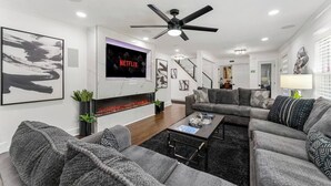 Ein modernes Wohnzimmer mit Kamin, Flachbildfernseher, Deckenventilator und einer Treppe, die zu einer weiteren Ebene führt.