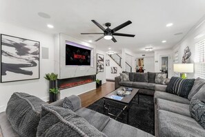 Un salon moderne doté d’une cheminée, d’un téléviseur à écran plat, d’un ventilateur de plafond et d’un escalier menant à un autre niveau.