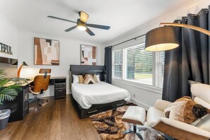 Een moderne slaapkamer met een bed, bureau, stoel en plafondventilator.