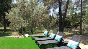 A row of dark-colored lounge chairs with blue and white cushions, arranged on a well-maintained green lawn, surrounded by trees. - 130m2 ground floor villa with private pool on 4000m2 of land (Les Arcs)