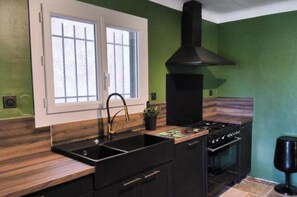 A kitchen with a black stove, a sink, and a window with white frames. - 130m2 ground floor villa with private pool on 4000m2 of land (Les Arcs)