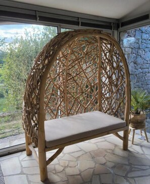 A wicker chair with a cushion, set on a stone floor, in a room with a stone wall and a window overlooking greenery. - 130m2 ground floor villa with private pool on 4000m2 of land (Les Arcs)
