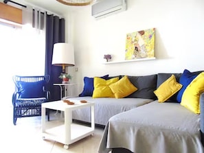 A hotel room with two beds, a white side table, a blue chair, and a painting on the wall. - 2 bed - Sleeps 4 - Balcony - City Centre (Faro)