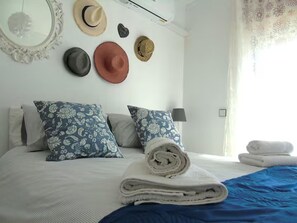 A neatly made bed with a blue and white striped bedspread, two pillows with floral patterns, a rolled white towel, and a mirror on the wall. - 2 bed - Sleeps 4 - Balcony - City Centre (Faro)