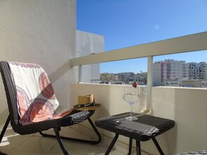 A balcony with a wicker chair, a small table, a glass of water, and a straw hat. - 2 bed - Sleeps 4 - Balcony - City Centre (Faro)