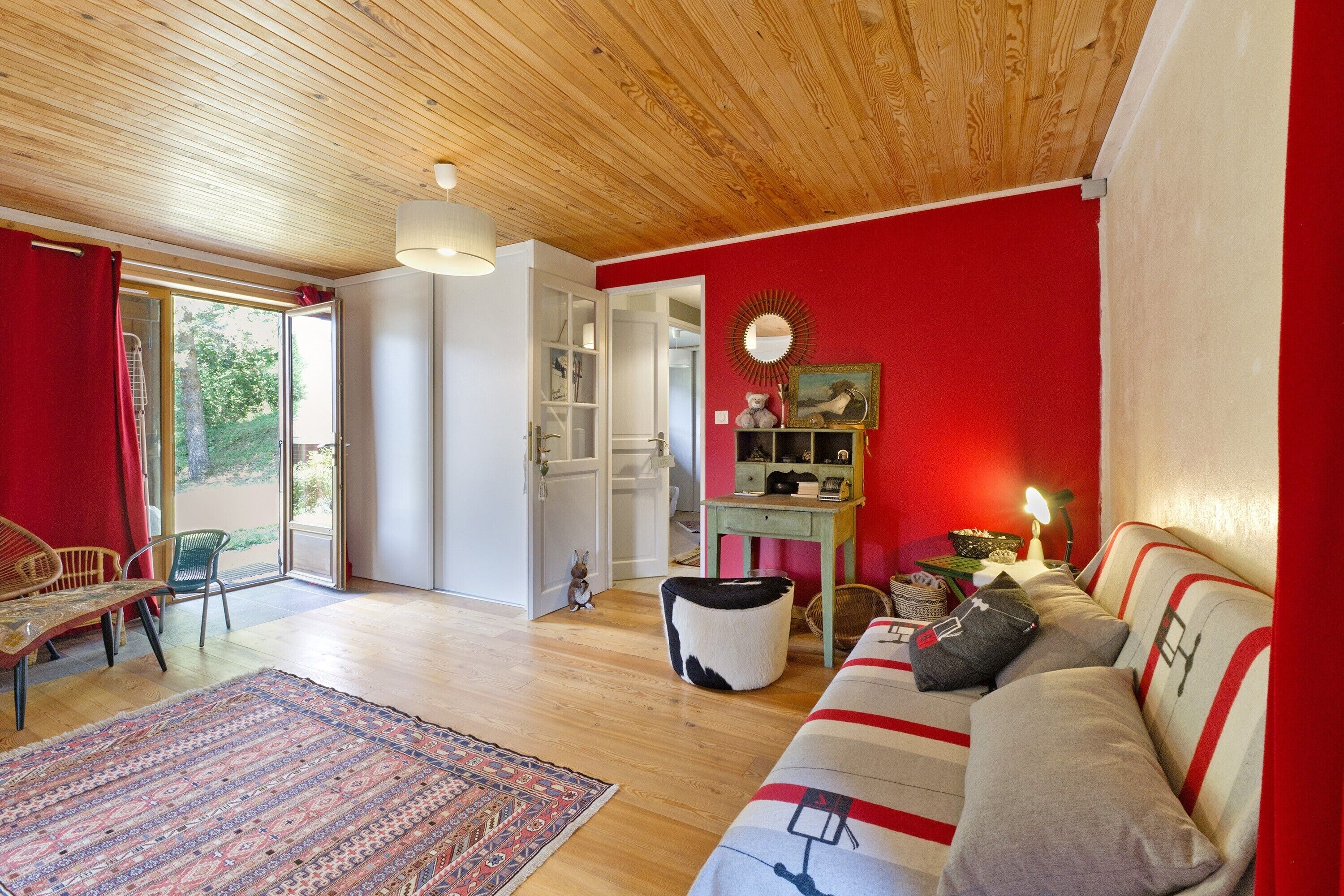 A living room with a wooden ceiling, a red wall, a sofa, a coffee table, and a patterned rug.