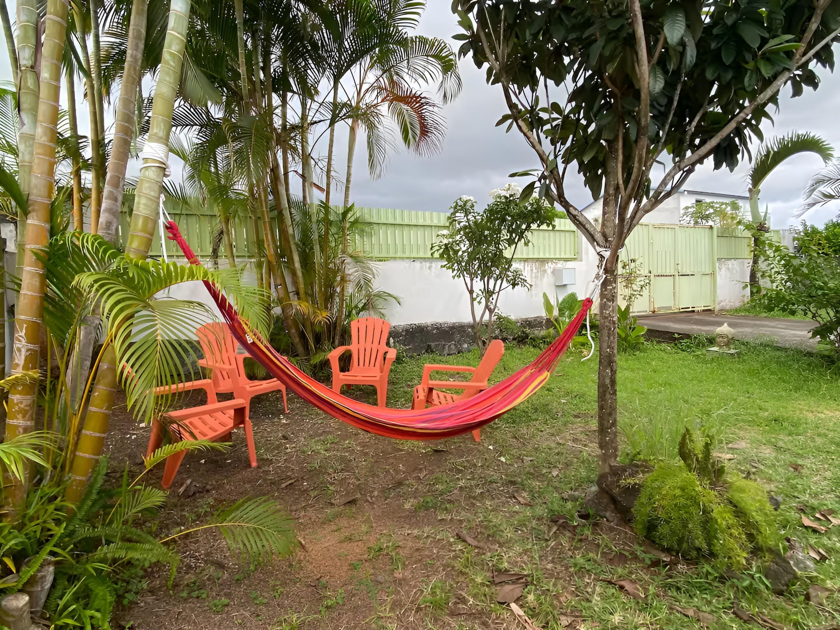 Un hamac tendu entre deux chaises orange, dans un jardin agrémenté de bambous et de palmiers.
