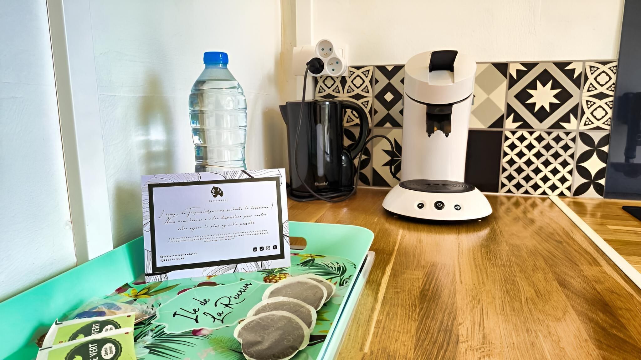 A kitchen with a coffee maker, a water bottle, and a laptop on a table.