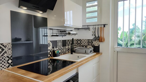A modern kitchen with a black induction cooktop, white cabinets, patterned backsplash, and a window with a view of greenery.