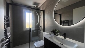 Une salle de bain moderne avec une douche à parois de verre, un lavabo blanc et un grand miroir.