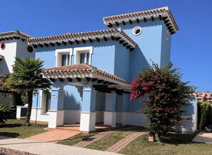 Un edificio azul con techo de tejas, una puerta y un ventanal pequeño.