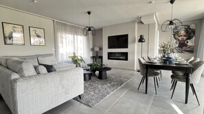Una sala moderna con un sofá gris, una mesa de comedor con sillas, un televisor de pantalla plana y obras de arte en las paredes.