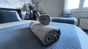Una cama bien hecha con una toalla enrollada, una mesita de noche con una lámpara y una ventana con cortinas.