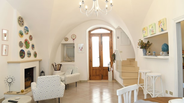 Uma sala de estar com lareira, poltronas estampadas, um candelabro e uma escadaria.