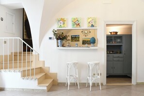 Eine Treppe führt zu einer Empore mit einer weißen Geländer, einem Regal mit Kunstwerken und einer Vase, sowie zu einem Küchenbereich mit Schränken und einem Topf.